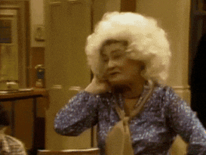 a woman wearing a wig and a blue shirt is sitting at a table .