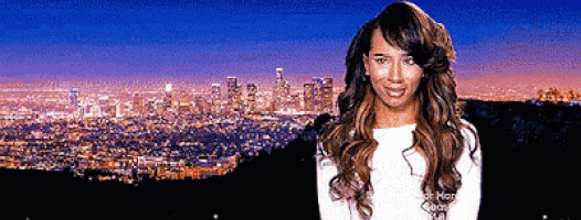 a woman is standing in front of a city at night