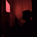 a person is sitting in front of a red curtain and looking at a cell phone .