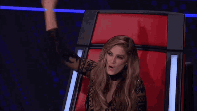 a woman is sitting in a red chair with her hand in the air .