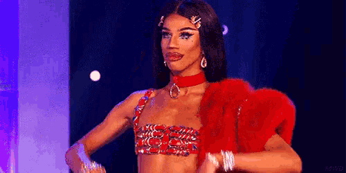 a drag queen is standing on a stage wearing a red top and fur coat .