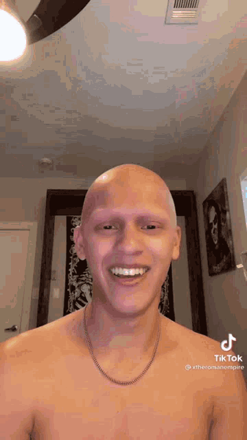 a shirtless man with a shaved head and no eyebrows is smiling .