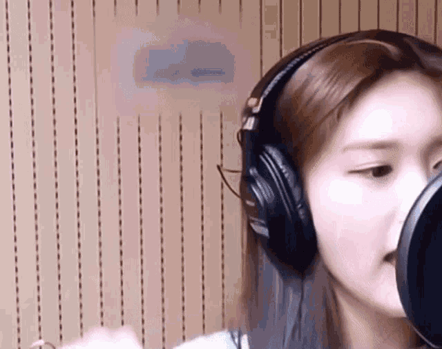 a woman wearing headphones is singing into a microphone in a studio .