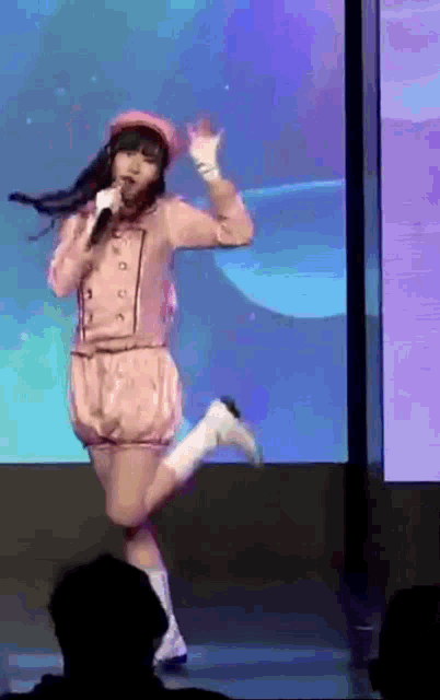 a girl in a pink outfit singing into a microphone on stage