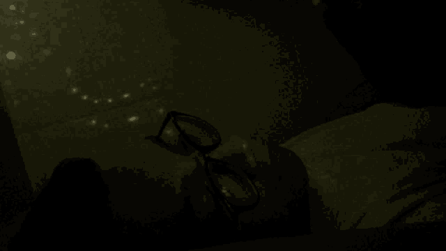 a man wearing glasses is laying in the dark