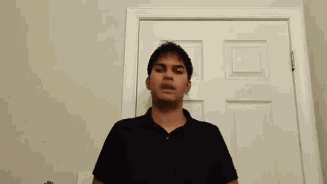 a young man in a black shirt is standing in front of a door .