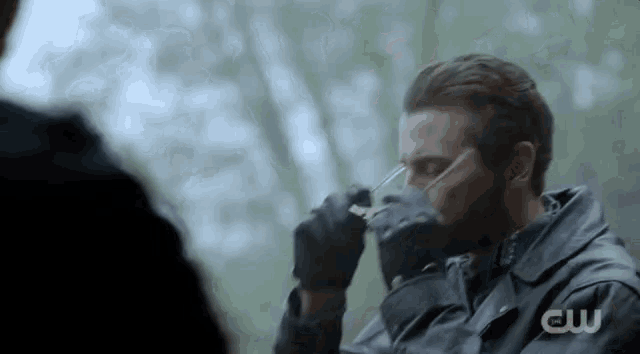 a man in a black jacket is drinking from a glass while talking to another man .