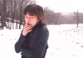a woman is smoking a cigarette in the snow while standing in the snow .