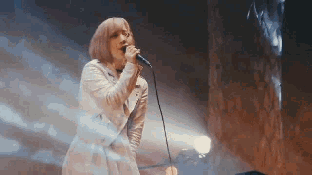 a woman in a white jacket is singing into a microphone on a stage .