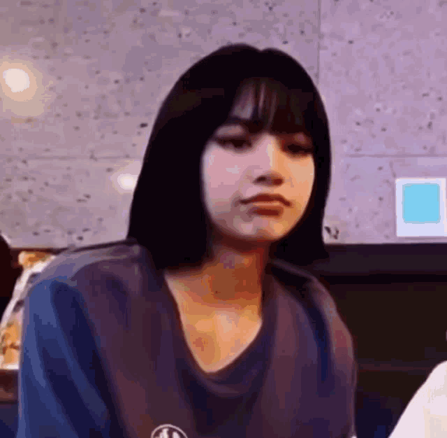 a woman with short black hair and bangs is wearing a blue t-shirt and making a funny face .