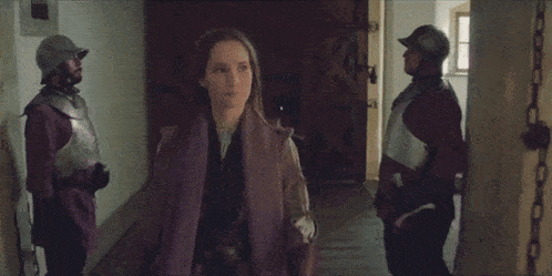 two women are walking down a hallway while a man in armor stands behind them .