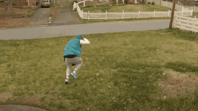 a man in a blue jacket is running down a street in front of a house