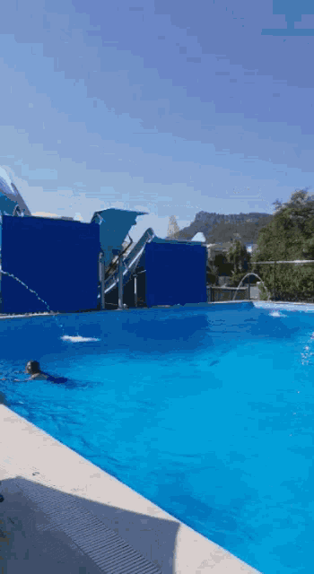 a person is swimming in a large pool with a water slide in the background
