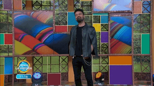 a man stands in front of a colorful wall with a sign that says venga la alegria