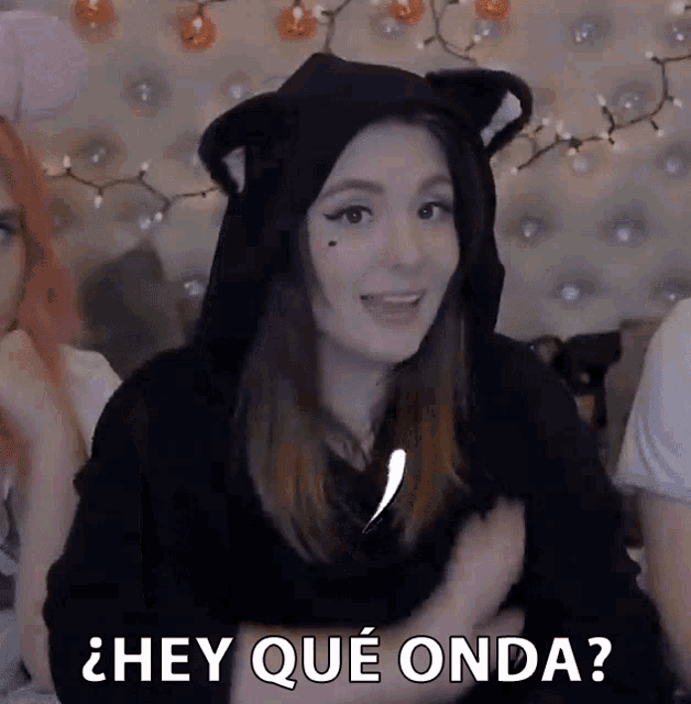 a woman wearing a cat ear hoodie says hey qué onda