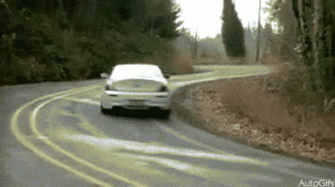 a white car is driving down a curvy road with trees in the background .