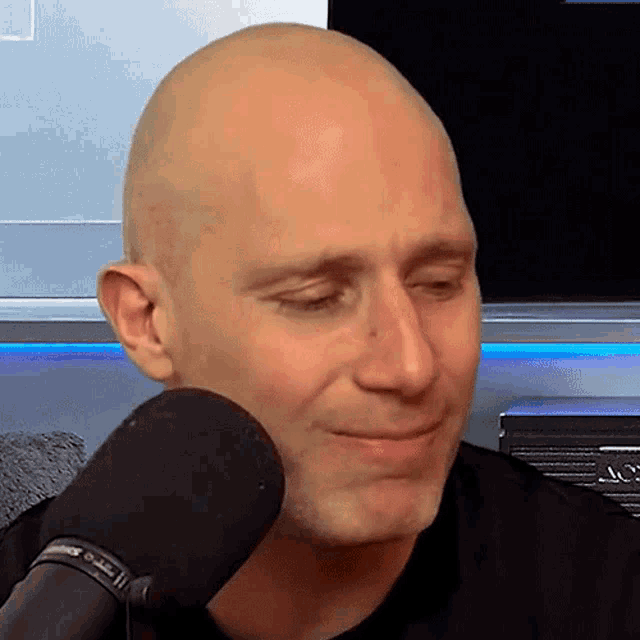a bald man is sitting in front of a microphone and smiling