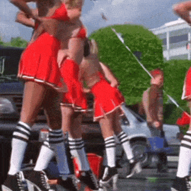 a group of cheerleaders in red skirts and striped socks are dancing in a parking lot