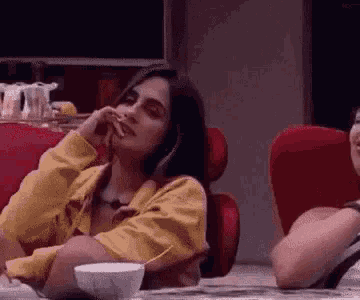 a woman in a yellow jacket is sitting in a red chair with her hand on her chin .