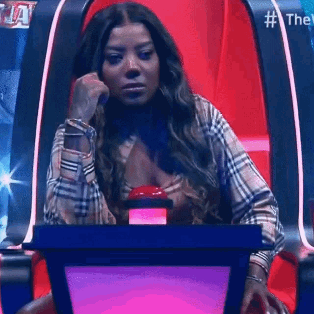 a woman in a plaid shirt is sitting in a chair with a red button in front of her ..