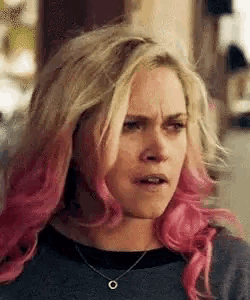 a woman with blonde and pink hair is wearing a necklace and making a funny face .
