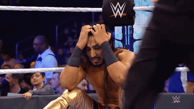 a wrestler in a wrestling ring holds his head in pain