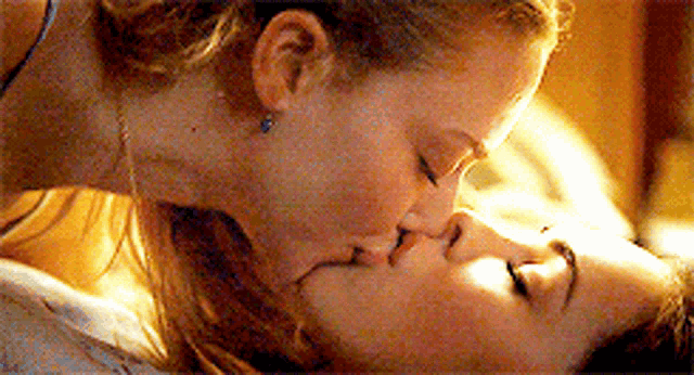 two women are kissing each other while laying down on a bed .