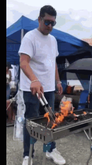 a man in a white shirt is grilling food on a barbecue grill .