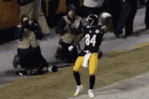 a football player with the number 84 on his jersey is dancing on the field while a crowd watches .