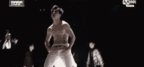 a man without a shirt is dancing on a stage with a mnet logo above him