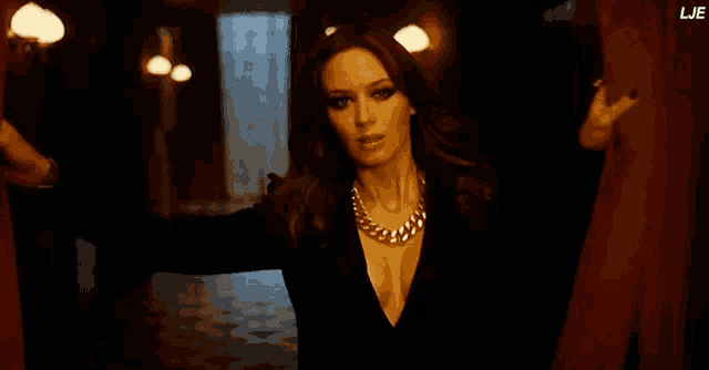 a woman in a black dress with a gold chain around her neck is standing in a dark hallway