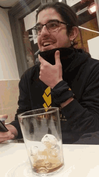 a man wearing glasses and a black shirt with a yellow arrow pointing at a glass with a skull in it