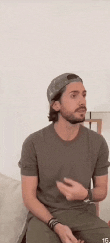 a man with a beard wearing a hat and a t-shirt is sitting on a couch .
