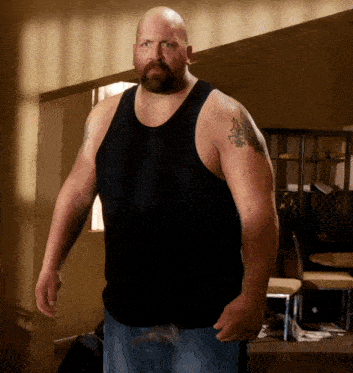 a bald man with a beard is wearing a black tank top and jeans