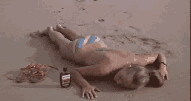 a woman in a bikini is laying on the sand on the beach .