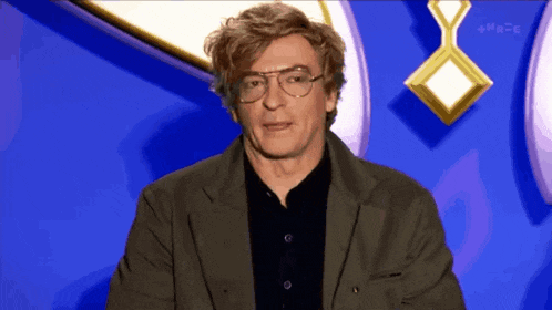 a man wearing glasses and a black shirt stands in front of a blue background