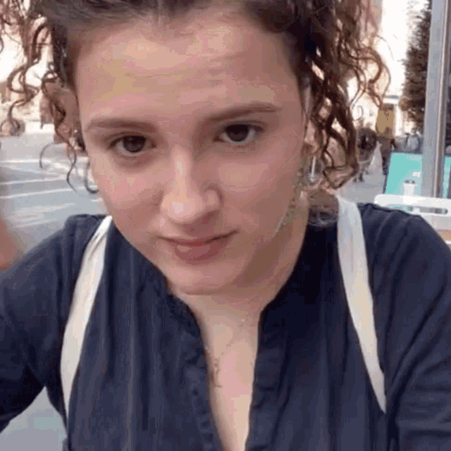 a woman with curly hair is wearing a blue shirt and a white backpack