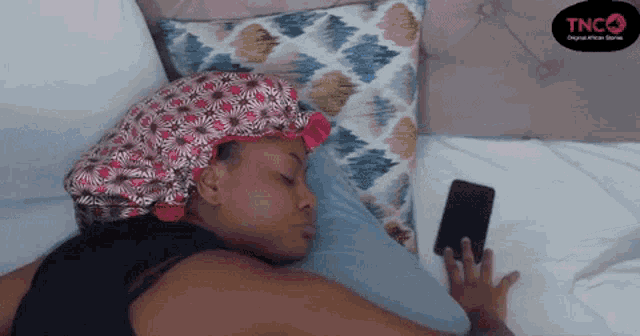 a woman wearing a bonnet is laying on a bed looking at her phone .
