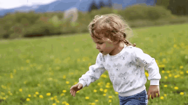 a little girl wearing a mickey mouse sweater is running through a field of flowers