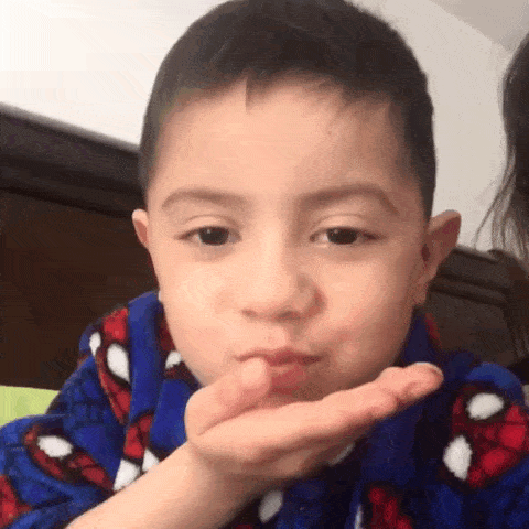 a young boy is blowing a kiss with his hand while wearing a spiderman pajama .
