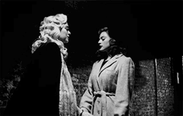 a black and white photo of two women standing next to each other holding hands .