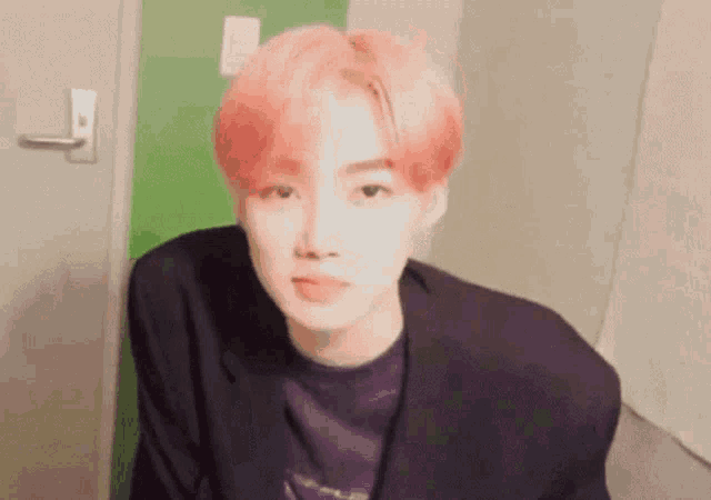 a young man with pink hair and a black jacket is sitting in front of a green door .