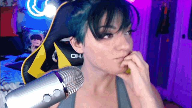 a woman with blue hair is sitting in front of a microphone with the word oh on her chair