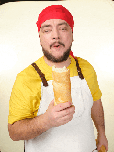 a man wearing a yellow shirt and white apron is holding a sandwich