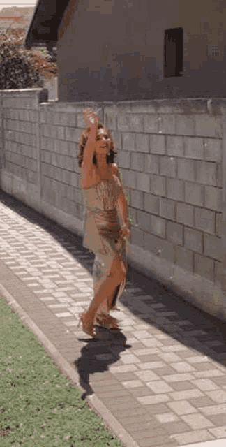 a woman in a dress is standing on a sidewalk next to a brick wall .