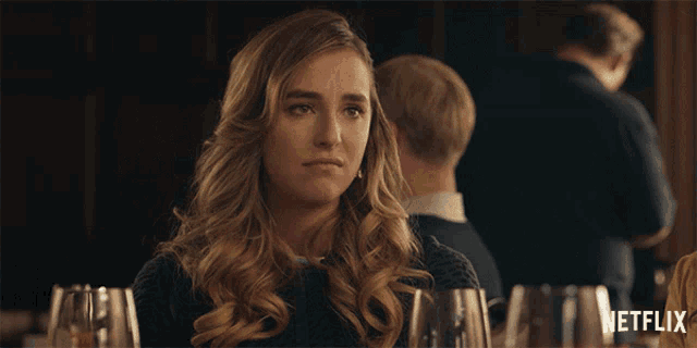 a woman sitting at a table with a netflix logo on the bottom right