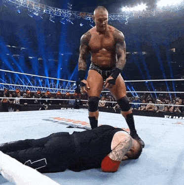 a wrestler standing over another wrestler laying on the floor