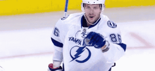 a hockey player wearing a white jersey with a lightning bolt on it is holding a puck on the ice .