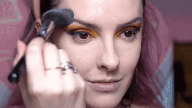 a woman with pink hair is applying makeup to her face .