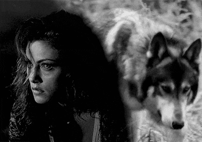 a black and white photo of a woman standing next to a husky dog .